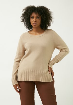 Beige sweater med lange ærmer og rund halsudskæring. Har ribbet tekstur ved kanten og ærmerne. Matcher med brune bukser.