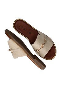 Beige geweven slidesandalen met een platte zool, gouden hardwareaccent en een bruine binnenzool. Getextureerde bovenkant en een contrasterend zoolontwerp.