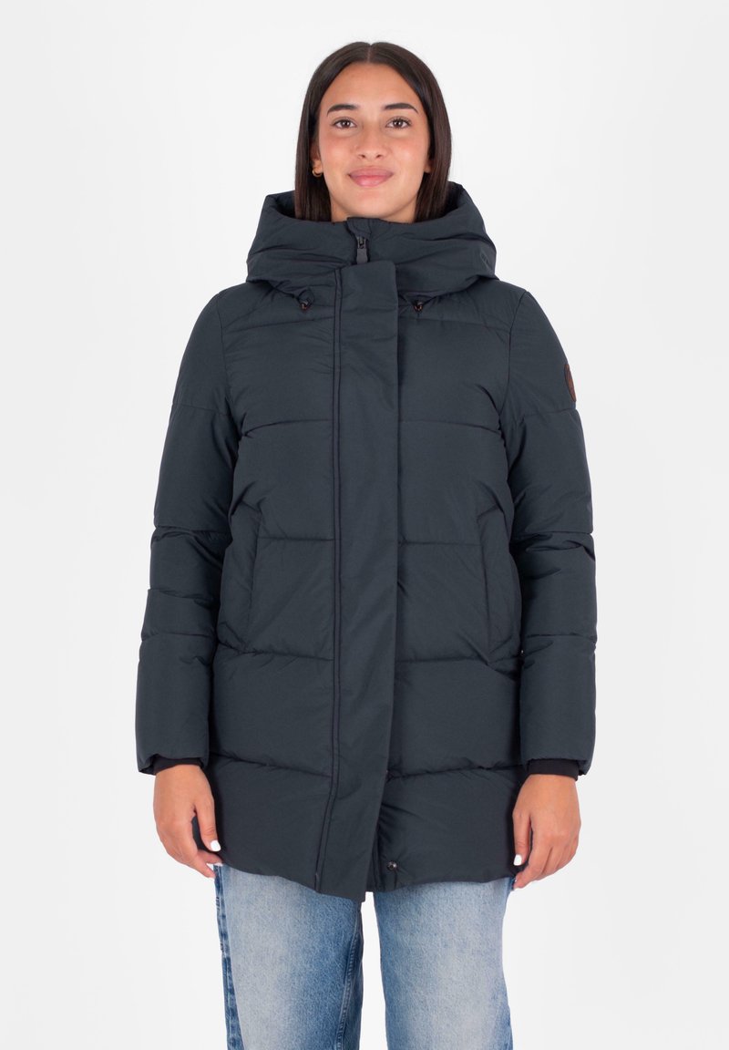 Donkerblauwe pufferjack met capuchon, voorzien van een gequilt ontwerp, ritssluiting en drukknoopsluitingen. Gecombineerd met casual lichtgewassen jeans.