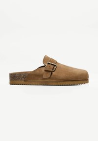 Barna velúr, slip-on klumpák csattal, parafa középtalppal és texturált gumitalppal. Lekerekített orr, minimalista dizájn.