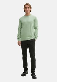 Maglione a maglia verde chiaro con scollo rotondo, abbinato a pantaloni grigio scuro e scarpe nere con lacci. Design semplice, texture morbida.