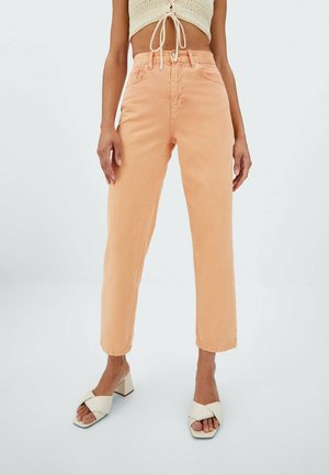 Úzké džíny broskvové barvy s vysokým pasem nošené s krémovými sandály na podpatku a krátkým pleteným topem uvázaným v pase.