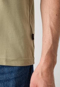Olivengrønn bomull T-skjorte med rett nederkant og sidesømsetter. Har en myk tekstur og korte ermer, kombinert med mørk denim.