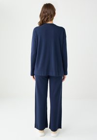 Maglione lavorato a maglia blu navy e pantaloni a gamba larga coordinati, realizzati in materiale morbido. L'outfit presenta una vestibilità comoda e maniche lunghe con un design semplice.