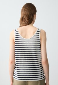 Gestreepte tanktop in crème en marineblauw, met een diepe ronde achterkant en smalle schouderbandjes. Zachte stof met een ontspannen pasvorm.