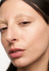 Närbild av ett ansikte med ljus hy, slät textur, lätt definierade drag, fylliga läppar och rakt mörkt hår. Inga synliga sminkprodukter.