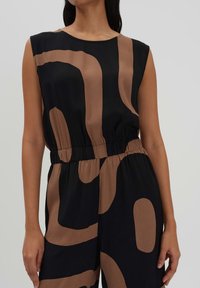 Zwarte mouwloze jumpsuit met abstracte bruine patronen, elastische tailleband en gladde textuur. Eenvoudige ronde halslijn en ruime pasvorm.