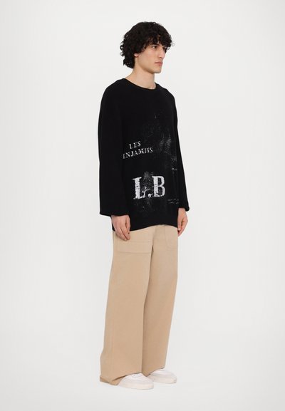 Pull noir surdimensionné avec texte imprimé blanc, associé à un pantalon large beige. Matière en coton, design décontracté et baskets.