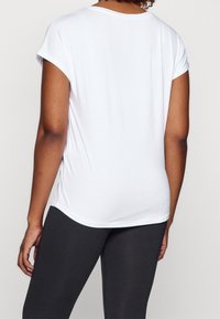 Biała koszulka z krótkim rękawem i okrągłym dekoltem, wykonana z miękkiej bawełny, o luźnym kroju, zestawiona z ciemnymi legginsami.