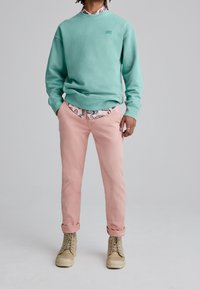 Mint green sweatshirt with ribbed cuffs, paired with pink pants and beige lace-up boots. Notable printed shirt peeks from beneath the sweatshirt.