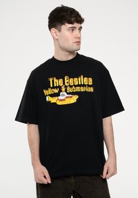 Black cotton t-shirt featuring a colorful graphic print of a yellow submarine with the text "The Beatles Yellow Submarine" in bold letters.
