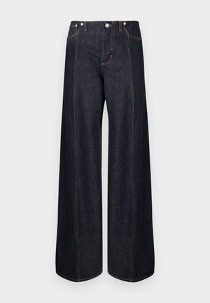 Tumed sinised laia lõikega teksad esitaskute, vööaasa ja oranži õmblusega, paigutatud valgele taustale.