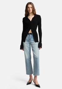 Cardigan a coste nera con colletto e bottoni, abbinato a jeans a gamba dritta blu chiaro e décolleté nere a punta.