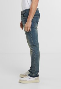 Slim-fit modré džíny s bledým umytím, dvě boční kapsy a klasický pětikapsový design. Nosit se bílé sportovní boty.