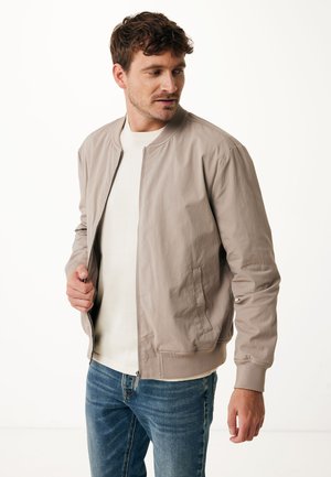 Veste bomber beige clair en tissu lisse, avec fermeture éclair à l'avant, poignets côtelés et coupe décontractée, associée à un jean bleu.