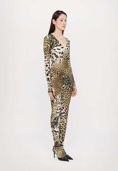 Jumpsuit z leopardjim vzorom, izdelan iz raztegljive tkanine, z globokim V-izrezom, dolgimi rokavi in prilegajočimi hlačami, v kombinaciji s črnimi špičastimi petami.