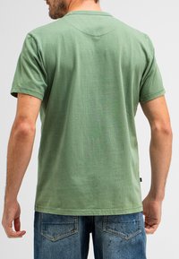 Groene korte mouwen t-shirt met ronde hals, lichte losse pasvorm en een gladde textuur. Gecombineerd met denim jeans met achterzakken.