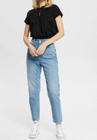 Haut noir à manches courtes avec un col en forme de goutte et des pois texturés, associé à un jean taille haute bleu clair et des baskets blanches.