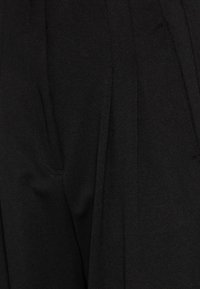 Zwarte broek van textuurstof, voorzien van plooien en zijzakken. Het ontwerp is strak met een op maat gemaakte pasvorm.