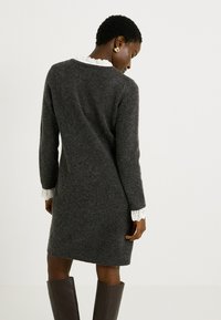 Vestido de lana gris con manga larga, que cuenta con un cuello y puños de encaje blanco. El vestido tiene un corte relajado, terminando por encima de la rodilla.