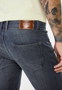 Donkerblauwe denim jeans met een bruine leren patch met een reliëflogo. Bevat twee achterzakken en subtiele stikdetails.