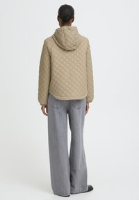 Bež prešita jakna s kapuco in stranskimi žepi, z zaobljenim robom. Kombinirana z sivimi kavbojkami širokih hlačnic.