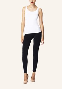 Vit linne i kombination med svarta leggings; modellen har på sig hudfärgade högklackade skor. Slät tyg med åtsittande passform och minimal detaljering.