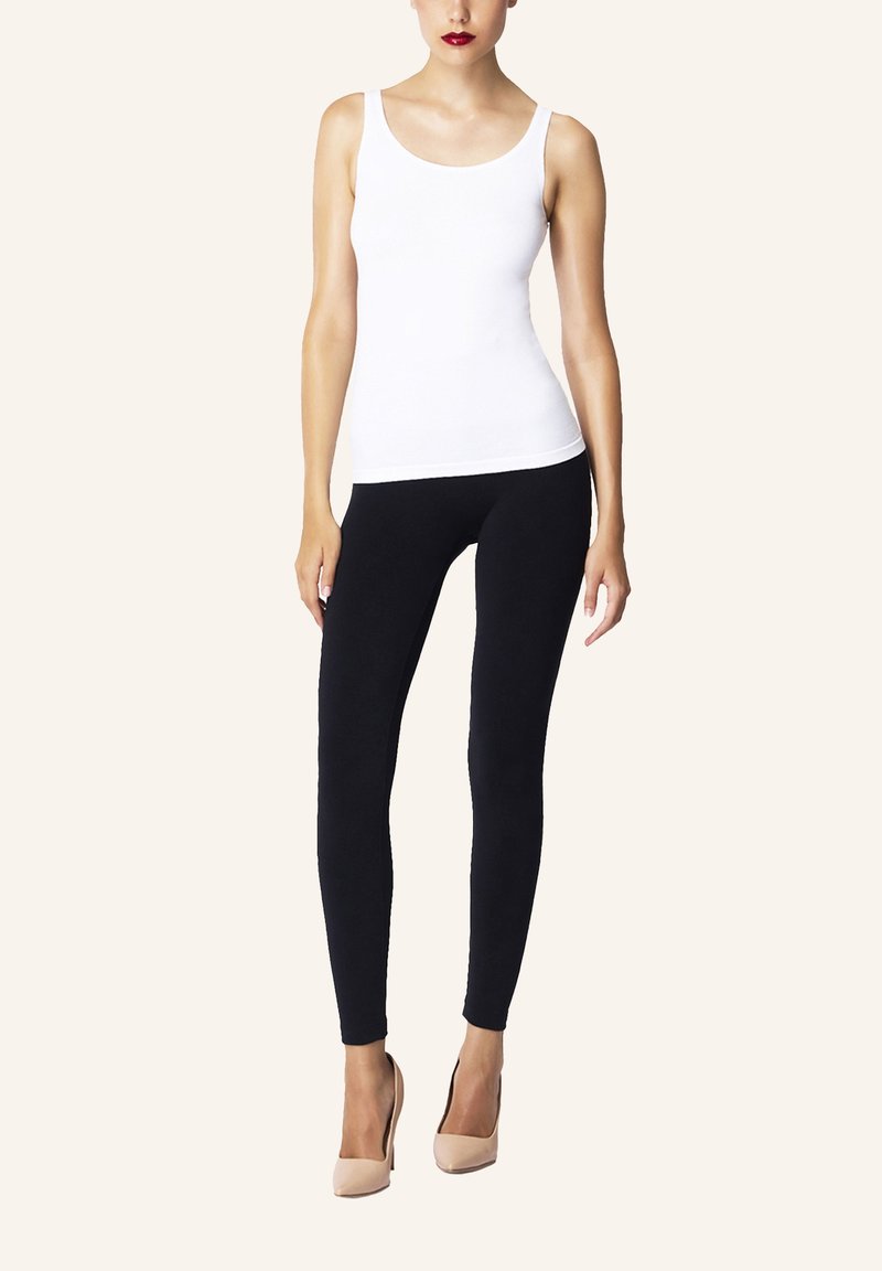 Vit linne i kombination med svarta leggings; modellen har på sig hudfärgade högklackade skor. Slät tyg med åtsittande passform och minimal detaljering.