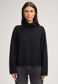 Maglione a collo alto nero in maglia con una vestibilità rilassata, polsini e orlo a coste, e tessuto testurizzato. Abbinato a jeans scuri.