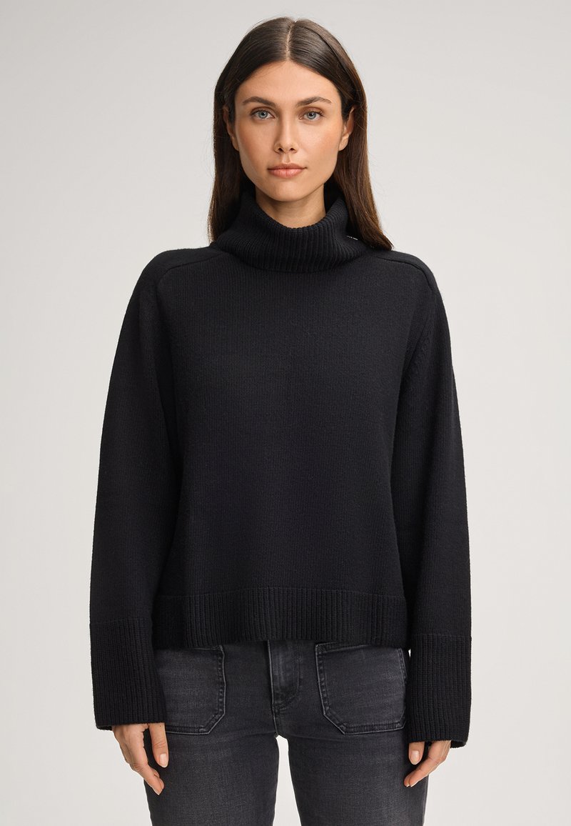 Maglione a collo alto nero in maglia con una vestibilità rilassata, polsini e orlo a coste, e tessuto testurizzato. Abbinato a jeans scuri.