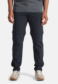 Pantaloni convertible neri realizzati in tessuto leggero, con cosce zip e polsini elasticizzati. Abbinati a sneakers grigie e una maglietta grigio scuro.