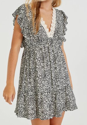 Mujer con un vestido de estampado floral en blanco y negro, con mangas cortas con volantes y un escote profundo en V rematado con encaje blanco.