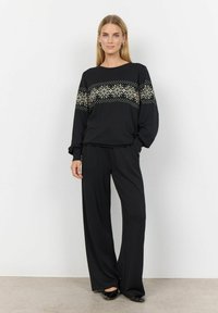 Zwarte blouse met lange mouwen en een decoratief gouden sterachtig patroon, met bijpassende zwarte wijde broek. Glad materiaal, ontspannen pasvorm en ronde halslijn.