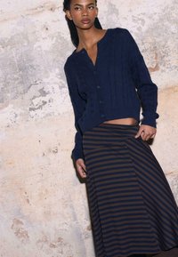 Granatowy kardigan z dzianiny w warkocze, z okrągłym dekoltem i guzikami, zestawiony z brązowo-granatową, paskowaną spódnicą o długości do kolan z drapowanym designem.