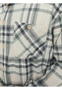 Langärmliges kariertes Hemd in Beige, Grün und Marineblau. Aus Baumwollmaterial mit einer Tasche, Knopfschluss und einem mehrdirektionalen Karomuster.