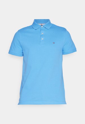 Light blue polo shirt made of cotton, featuring a collar, three buttons, and a small logo on the left chest. Short sleeves with ribbed cuffs.