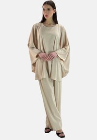 Completo beige a due pezzi composto da una blusa ampia e fluida con maniche larghe e pantaloni a gamba larga coordinati, realizzati in tessuto liscio.