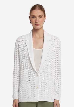 Vit öppen stickad cardigan med sjalkrage, två framfickor och knappstängning. Har ribbade ärmslut och fåll för extra textur.