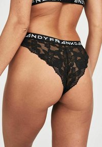String neri in pizzo con motivo floreale, dotati di una fascia morbida in vita con branding "FRANKIE", che mette in evidenza dettagli intricati e una trama trasparente.