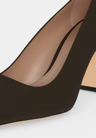 Gros plan sur un escarpin marron foncé avec une semelle intérieure en cuir beige et une fine bordure noire.
