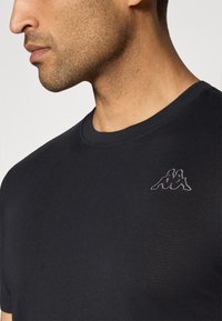 Zwart katoenen T-shirt met een ronde hals en korte mouwen, met een klein geborduurd logo op de linkerborst. Gladde textuur.