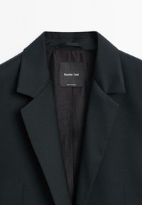 Černé sako s klopovým límcem, charakterizované hladkou texturou a tkanou látkou. Uvnitř je štítek s nápisem "Massimo Dutti."