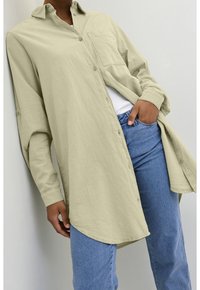 Chemise à manches longues vert clair à boutons, avec une poche poitrine, un ourlet arrondi et une texture douce, assortie à un jean bleu ajusté.