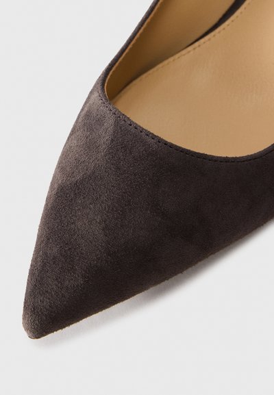 Chaussure plate en daim brun foncé à bout pointu, avec un intérieur en cuir lisse tan, présentée sur un fond blanc.