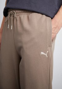 Braune Sweatpants aus weichem Stoff, mit einem elastischen Bund und seitlichen Taschen. Ein weißes Puma-Logo ist auf dem Oberschenkel gestickt.