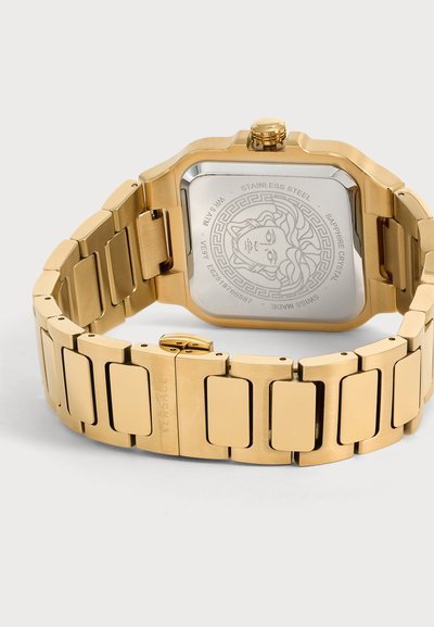 Montre-bracelet en métal doré avec bracelet à maillons, affichant le logo Médusa gravé et un fond en acier inoxydable avec des marquages détaillés.