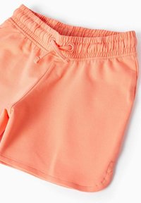 Pantaloni corti in cotone arancione con elasticizzato in vita e cordoncino. Texture liscia, tasche laterali e orlo cucito.