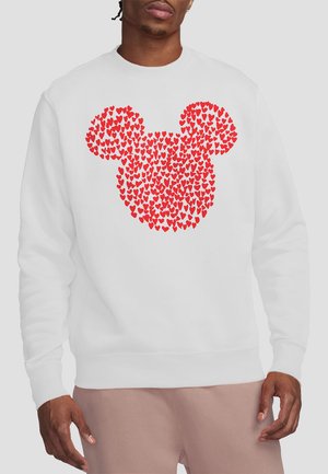 Man wearing white sweatshirt with red heart shapes forming a mouse head silhouette on the front.