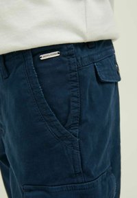 Pantaloni cargo blu navy in cotone, con tasche laterali, dettagli di cucitura e un piccolo tag metallico del marchio sulla vita.