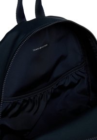 Svart ryggsäck inuti med slät tyg, elastisk ficka och varumärkesetikett. Dragkedjedetaljen vid kanten kompletterar designen.